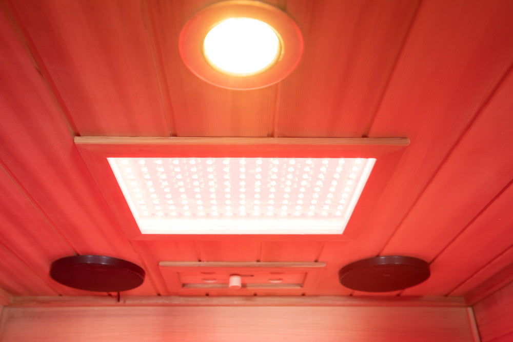 WizziSaunas SR01 Red Cedar Infrared Sauna interior ceiling view showing full spectrum heater panel glowing white chromotherapy ceiling light and two Bluetooth speakers in red light